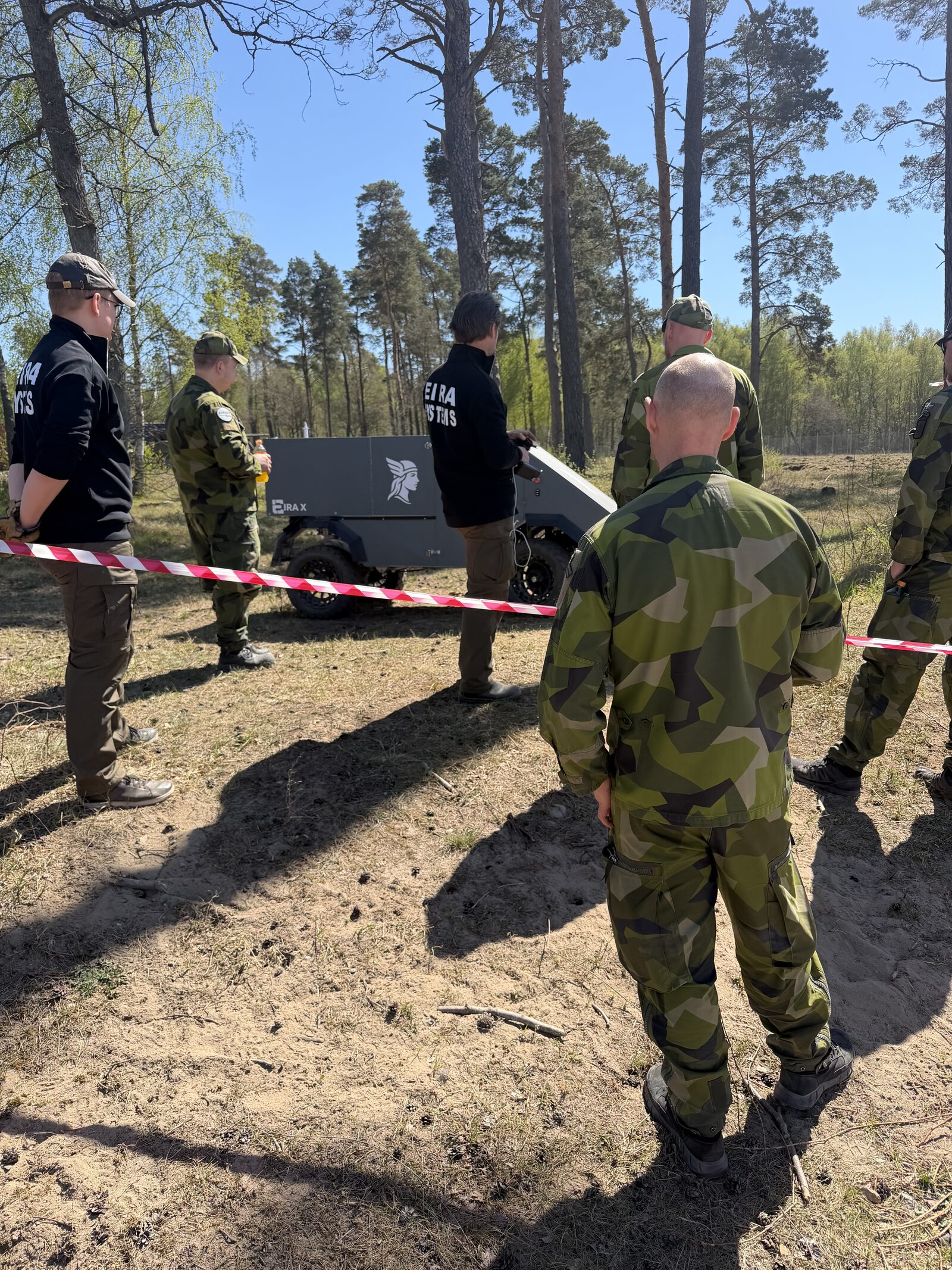 Eira team demonstrating to soldiers in M90 camouflage in a forest.