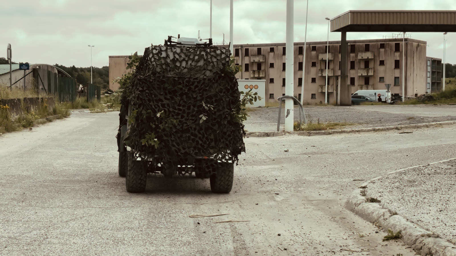 A camouflage-netted vehicle on the road past an abandoned fuel station